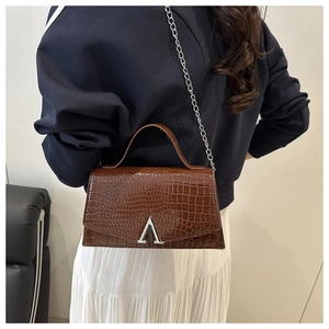 Detail of a brown crocodile pattern handbag with a silver V-shaped buckle and metal chain