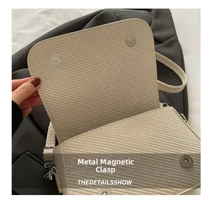 Detail view of the metal magnetic clasp and woven texture on a beige shoulder bag