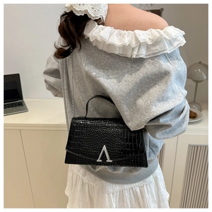 Detail of black crocodile texture handbag with silver A-shaped metal buckle and chain strap