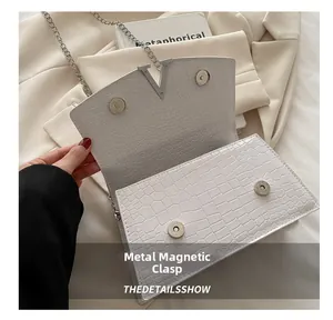 Detail of white crocodile embossed leather bag featuring silver V-shaped metal and magnetic snaps