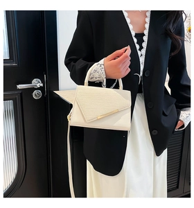 Detail of cream-white handbag with textured flap and gold metal bar on a black blazer