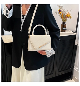 Detail of cream white leather handbag with asymmetric gold trim and slim shoulder strap