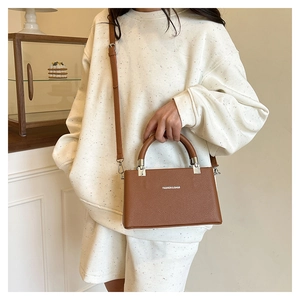 Close-up of brown litchi pattern leather handbag featuring a round handle and fine strap