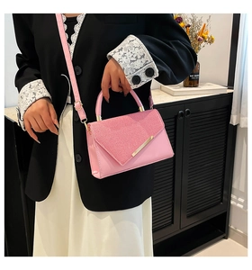 Detail of pink square handbag with rhinestone flap and gold trim worn by a model