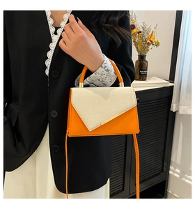 Detail of orange and beige handbag with woven flap and gold metal bar accent