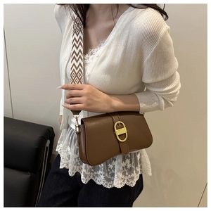 Detail view of brown baguette bag featuring a woven strap and gold D-shaped buckle