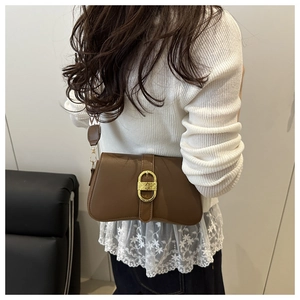 Close-up of a brown leather shoulder bag with a gold buckle worn on a white knit sweater