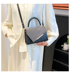 Detail view of contrast black and grey handbag with gold metal trim and adjustable strap