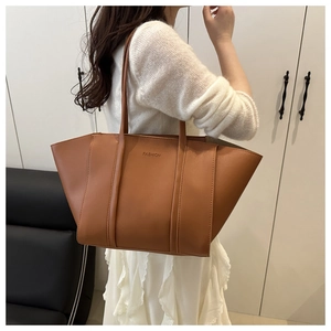 Detail view of large brown faux leather tote bag with FASHION embossed logo and slim straps