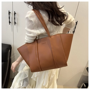 Detailed view of the brown leather tote bag with FASHION embossment shown on shoulder
