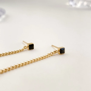 Detail of elegant gold drop earrings featuring black zircon studs and long chain tassels
