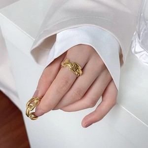 Detailed view of hollow chain rings in gold on hand with elegant white silk sleeves