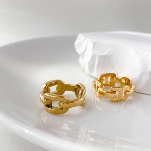 Detailed view of gold chain link rings on a white minimalist stone backdrop