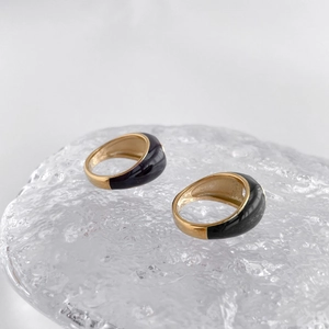 Close-up of golden Mobius rings with black enamel on a textured ice-like surface