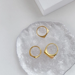 Tres anillos geométricos dorados con superficies facetadas en bandeja de vidrio