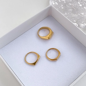Primer plano detallado de tres anillos cuadrados geométricos dorados en un joyero blanco