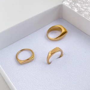 Vista macro de tres anillos geométricos dorados minimalistas en una caja de regalo blanca