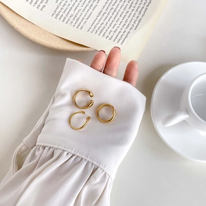 Detailed view of three polished 18K gold-plated minimalist rings on a white shirt cuff
