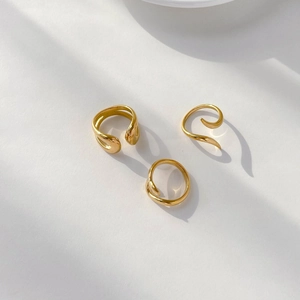 Three minimalist 18K gold plated fluid rings with a polished mirror finish on a cream background