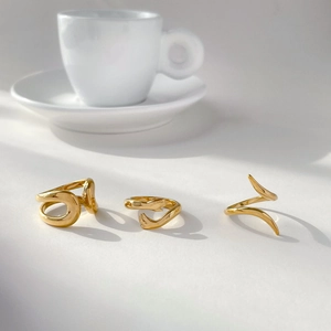 Three 18K gold plated rings including abstract snake and hug designs on white surface