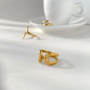 Macro detail of polished 18K gold plated abstract wavy ring on white display