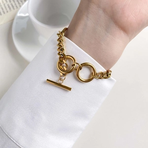 Close-up of golden chunky chain bracelet with toggle clasp over a white shirt sleeve