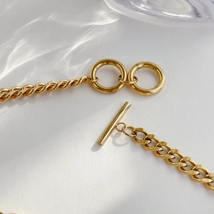 Macro detail of asymmetric gold chain link necklace with a decorative OT toggle clasp
