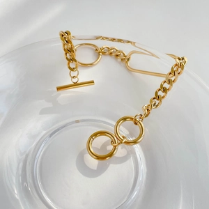 Detail of gold chunky link chain bracelet with OT toggle clasp on a glass bowl edge
