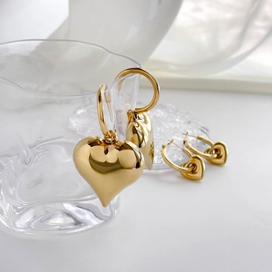 Polished gold heart drop earrings and nested studs set displayed on a glass