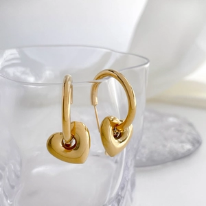 Detailed view of polished gold heart drop earrings hanging on a transparent glass edge