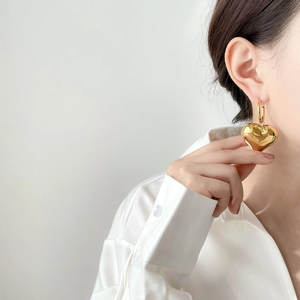 Close-up of a large oversized gold hollow heart pendant earring with polished finish