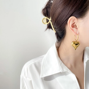 Close-up of golden hollow heart-shaped earrings and minimalist metal hair claw on a model