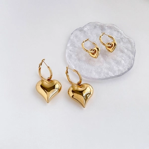Exaggerated golden heart-shaped hoop earrings with mirror polished finish on white backdrop
