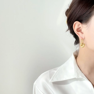 Close-up of a model wearing vintage gold hollow heart drop earrings on a white background