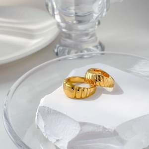 Paire de bagues torsadées larges dorées minimalistes sur fond de pierre blanche