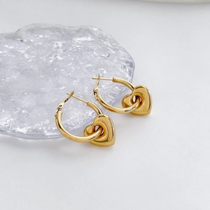 Polished gold heart drop earrings on a textured glass tray with minimalist background