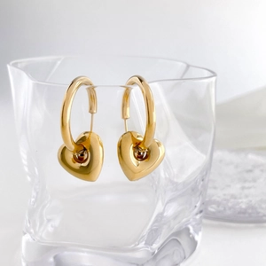 Close-up of golden hollow heart earrings hanging on a textured glass rim