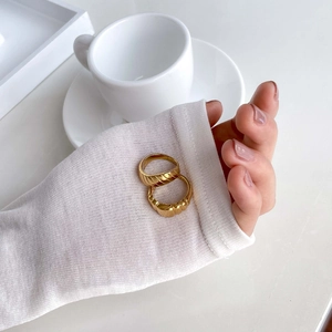 Détail de bagues dorées de style croissant portées avec une manche en maille blanche