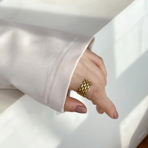 Détail d'une bague chaîne tissée dorée minimaliste portée à l'index avec une texture luxueuse