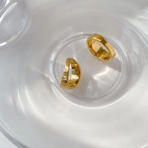 Vue détaillée de deux bagues torsadées dorées dans un bol en verre et ombres de lumière