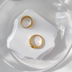 Détail de bagues dorées torsadées et perlées sur pierre blanche dans du verre