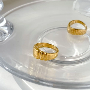 Détail de deux bagues dorées torsadées aux textures gaufrées sur plateau en verre
