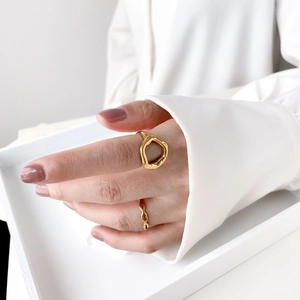 Close-up of a model wearing gold wavy and abstract lip rings over a white shirt