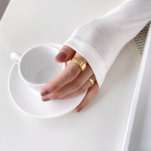 Gros plan d'une bague dorée à côtes larges et d'un anneau fin portés avec une tasse de café