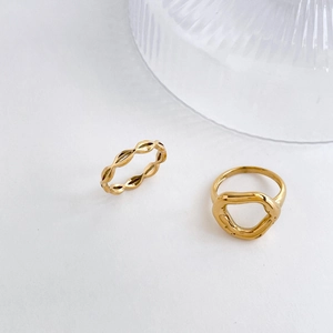 Detailed view of gold plated wavy band and abstract geometric hollow lip ring on white surface