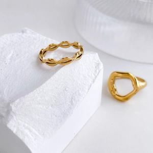 Close-up of polished gold stackable rings with wavy textures on a white stone background