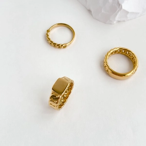 Detailed view of three gold chain-link style rings on a minimalist white stone background