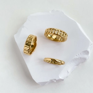 Three-piece gold Cuban link chain rings displayed on minimalist white stone platform