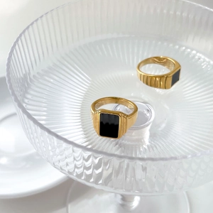 Détail de bagues chevalières dorées vintage avec onyx noir sur plateau en verre strié