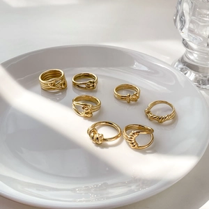 Set of seven gold twisted knot rings displayed on a white ceramic plate with warm lighting